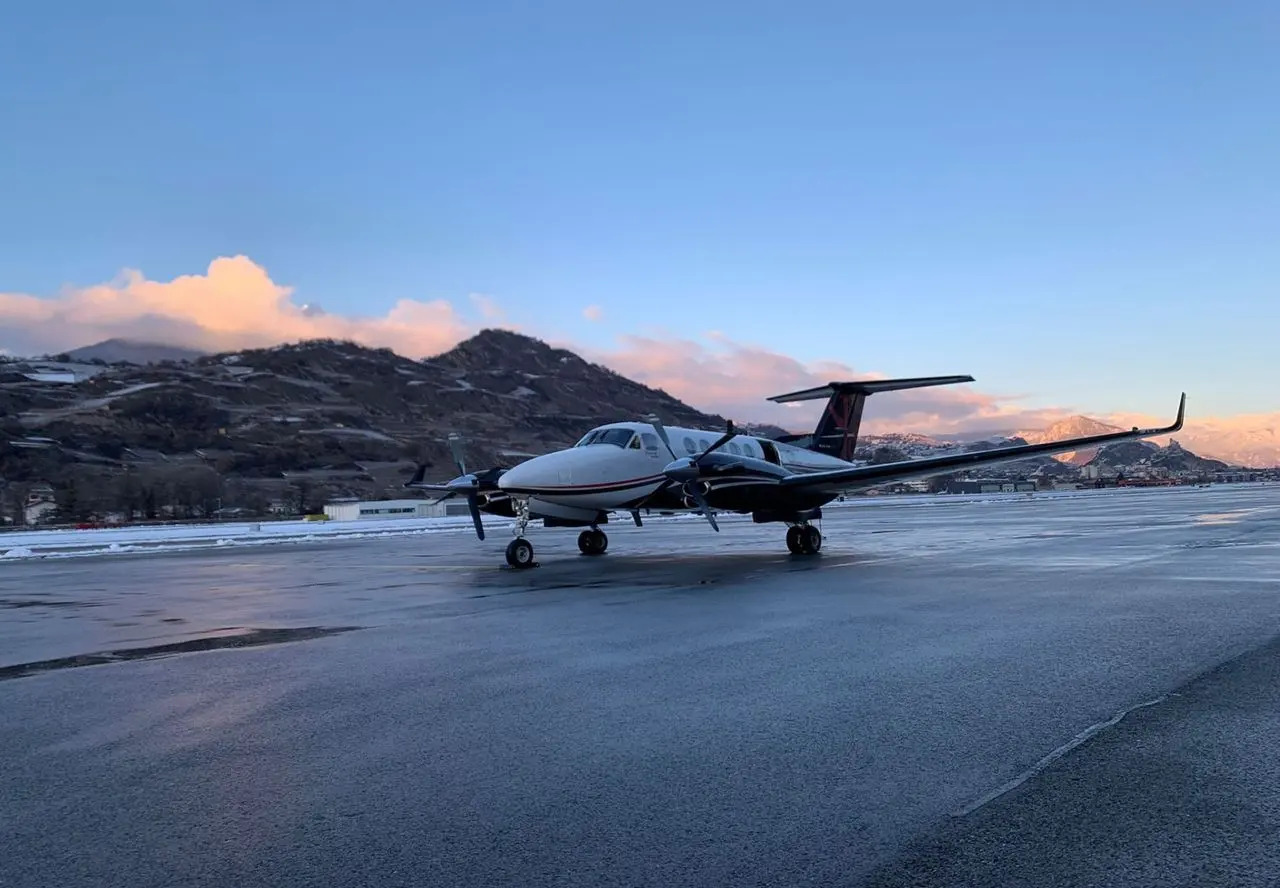 Twin-engine turboprop air taxi parked on the apron at dusk with hills behind
