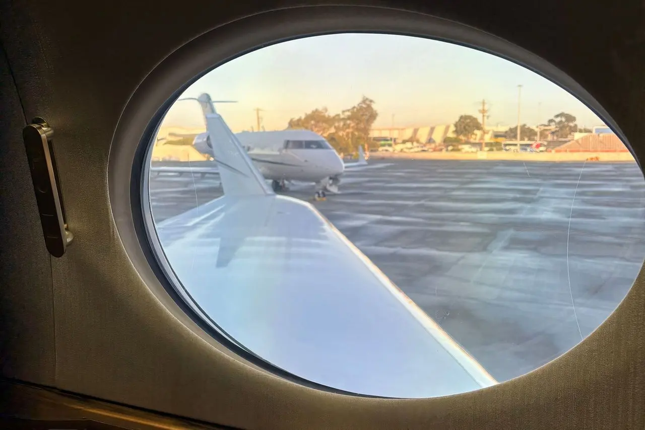 Looking out of a private jet cabin window at the apron in the evening light