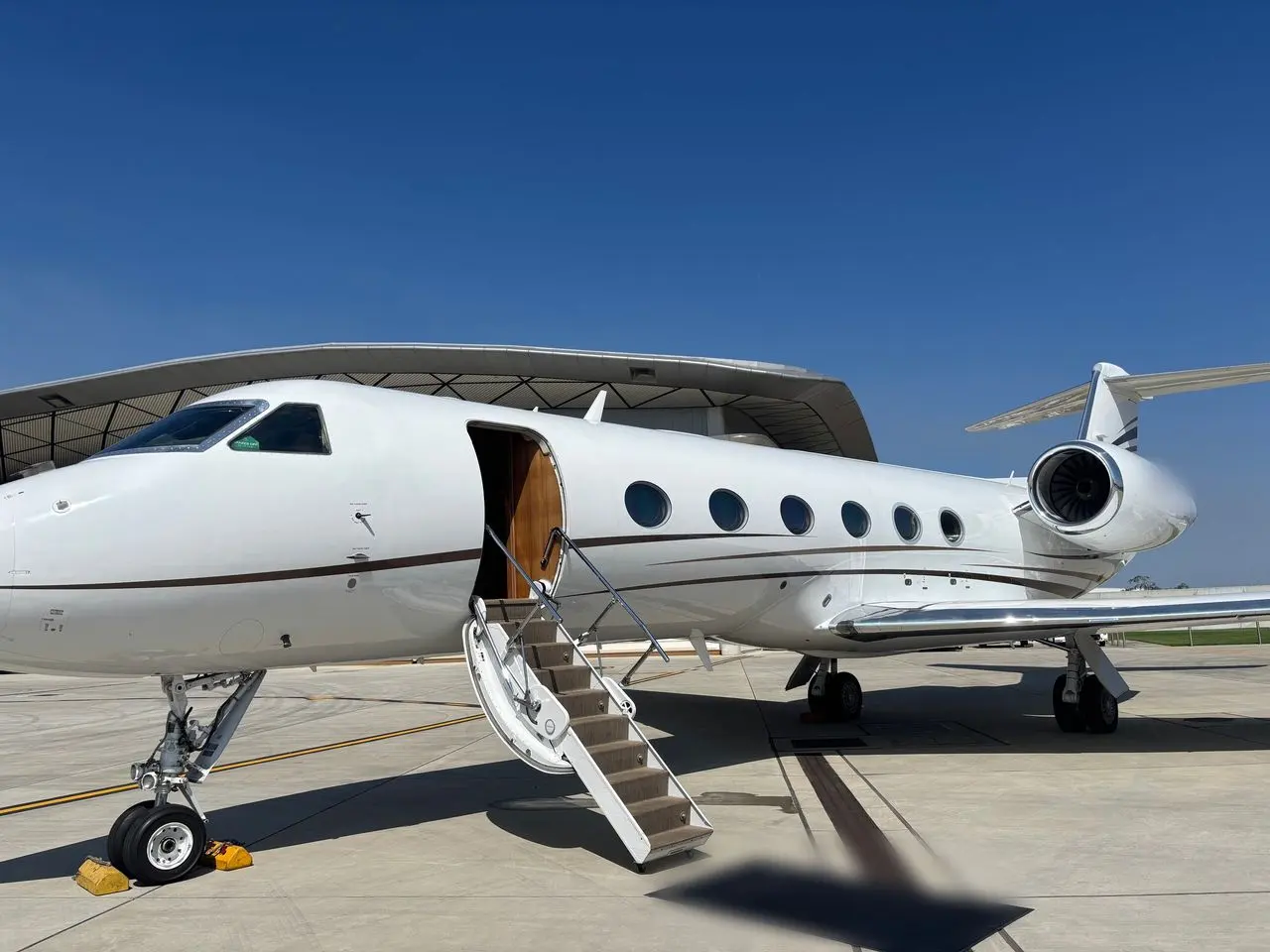 Large-cabin private jet with its airstair lowered outside a hangar under a deep blue sky