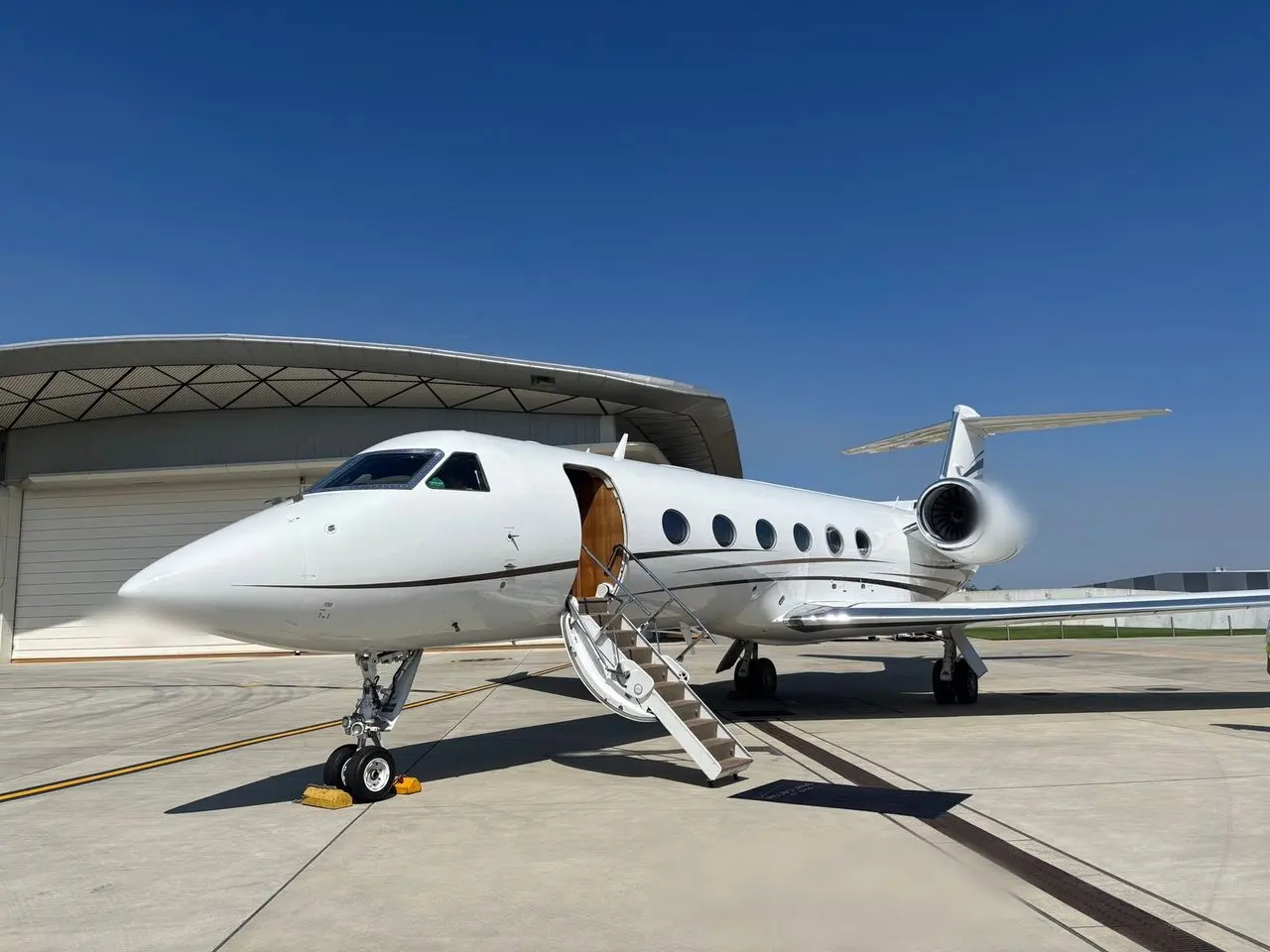 White large-cabin private jet with its airstair down in front of a hangar