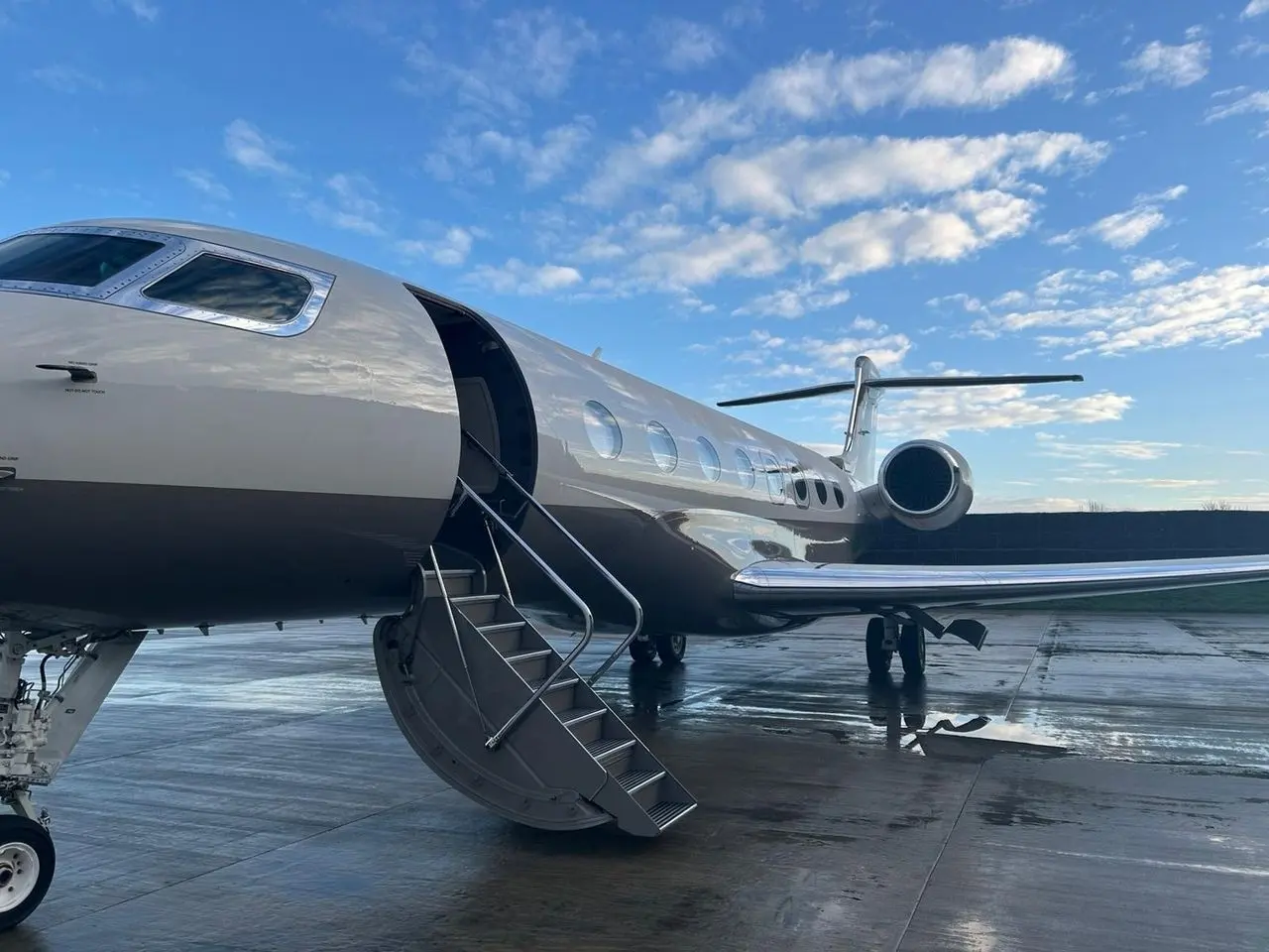 Silver large-cabin private jet with its airstair down on a wet apron after rain