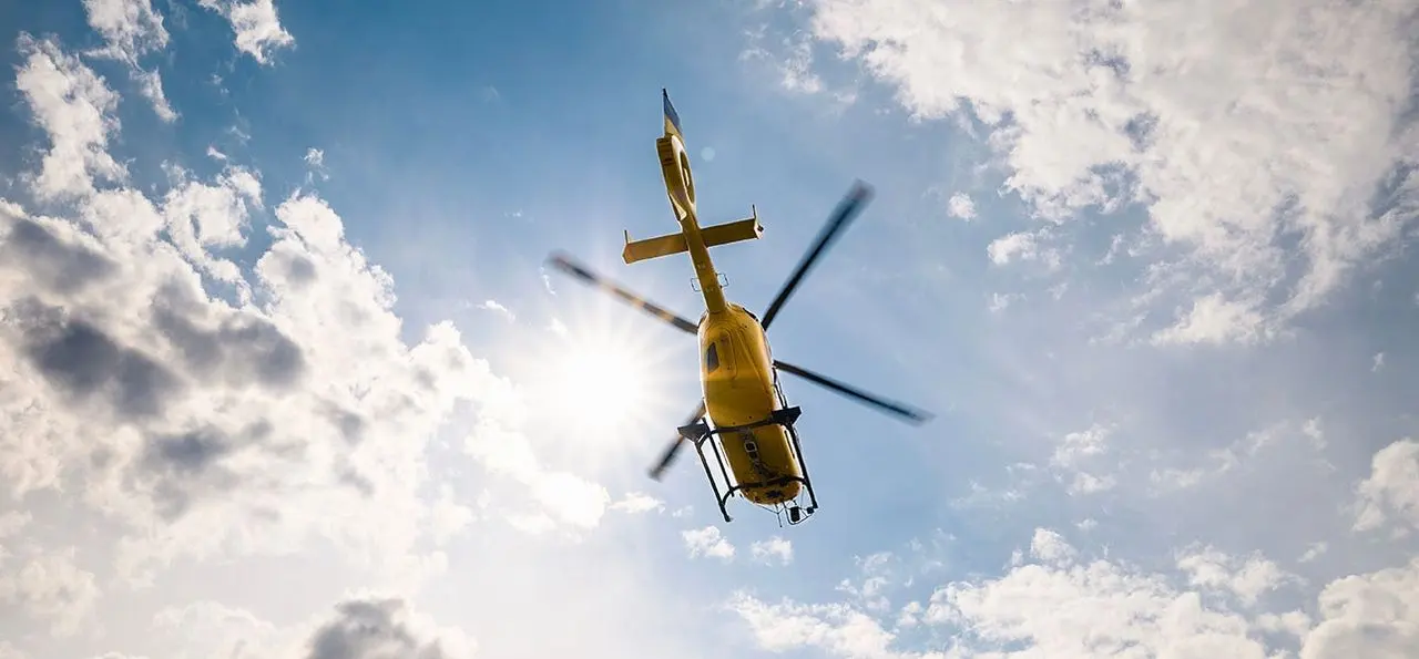 A helicopter flying against a blue sky with cloud