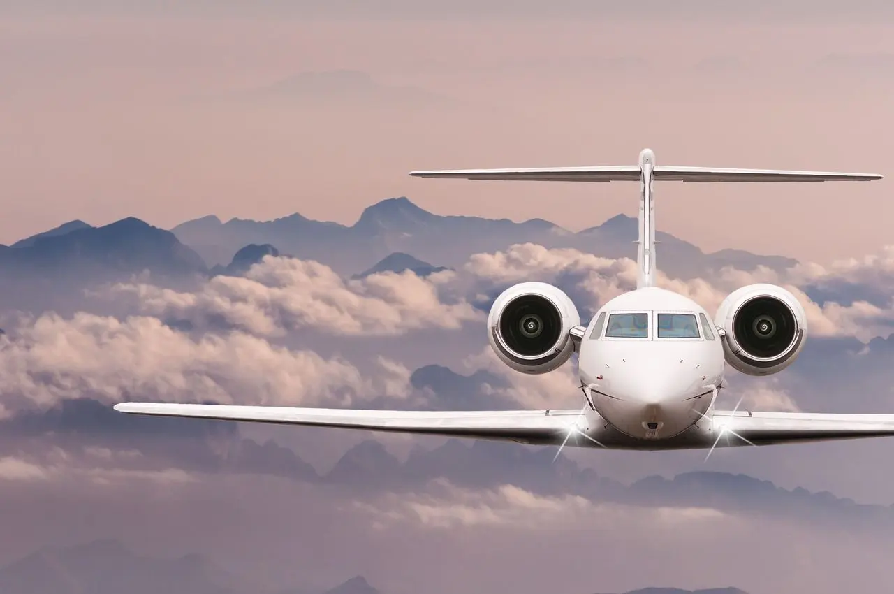 Private jet flying head-on above mountains at dusk