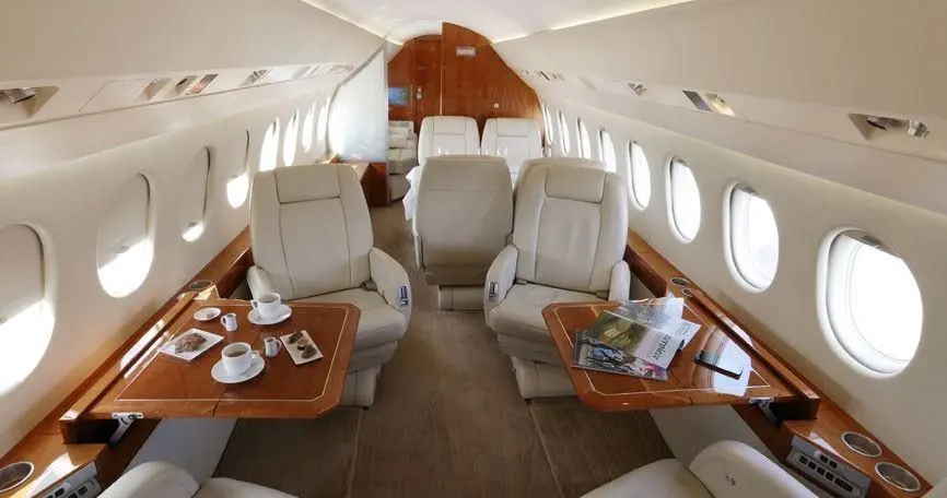 Private jet cabin with cream leather seats and a polished wood dining table