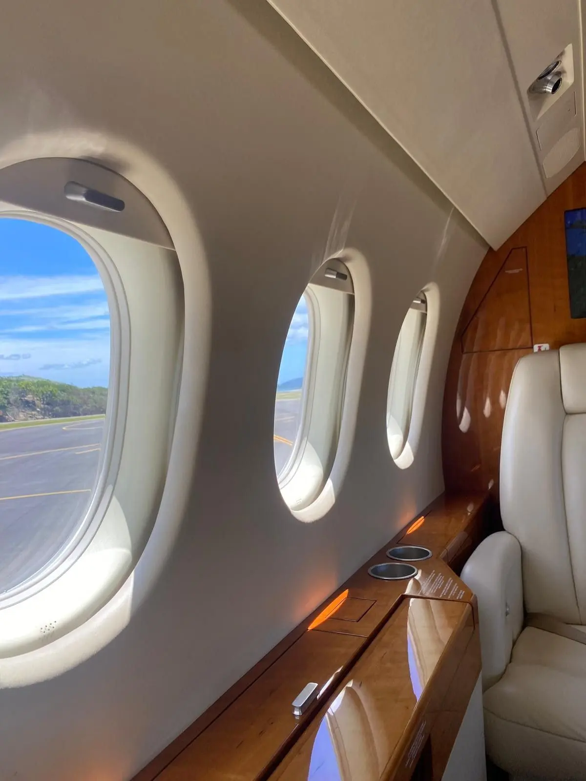 Private jet cabin windows and cream leather seat with a view over the airfield