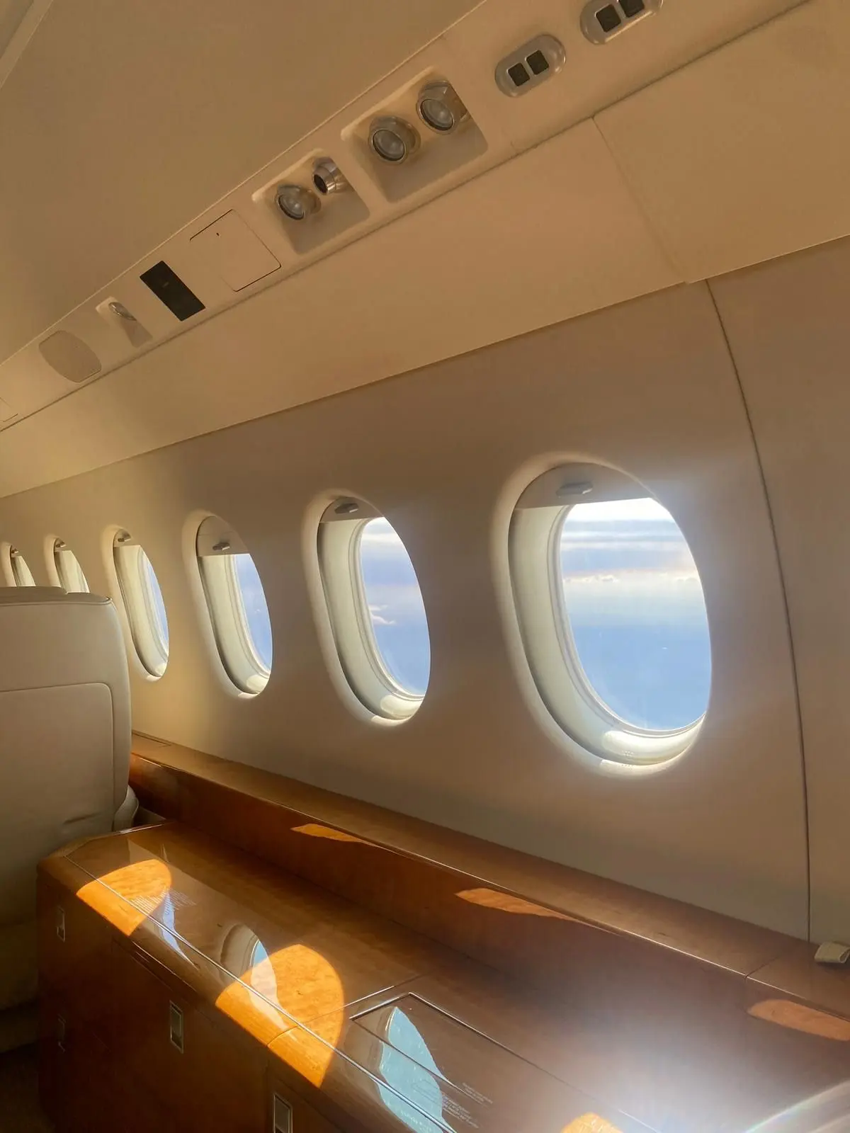 Row of oval cabin windows beside polished wood panelling in a private jet