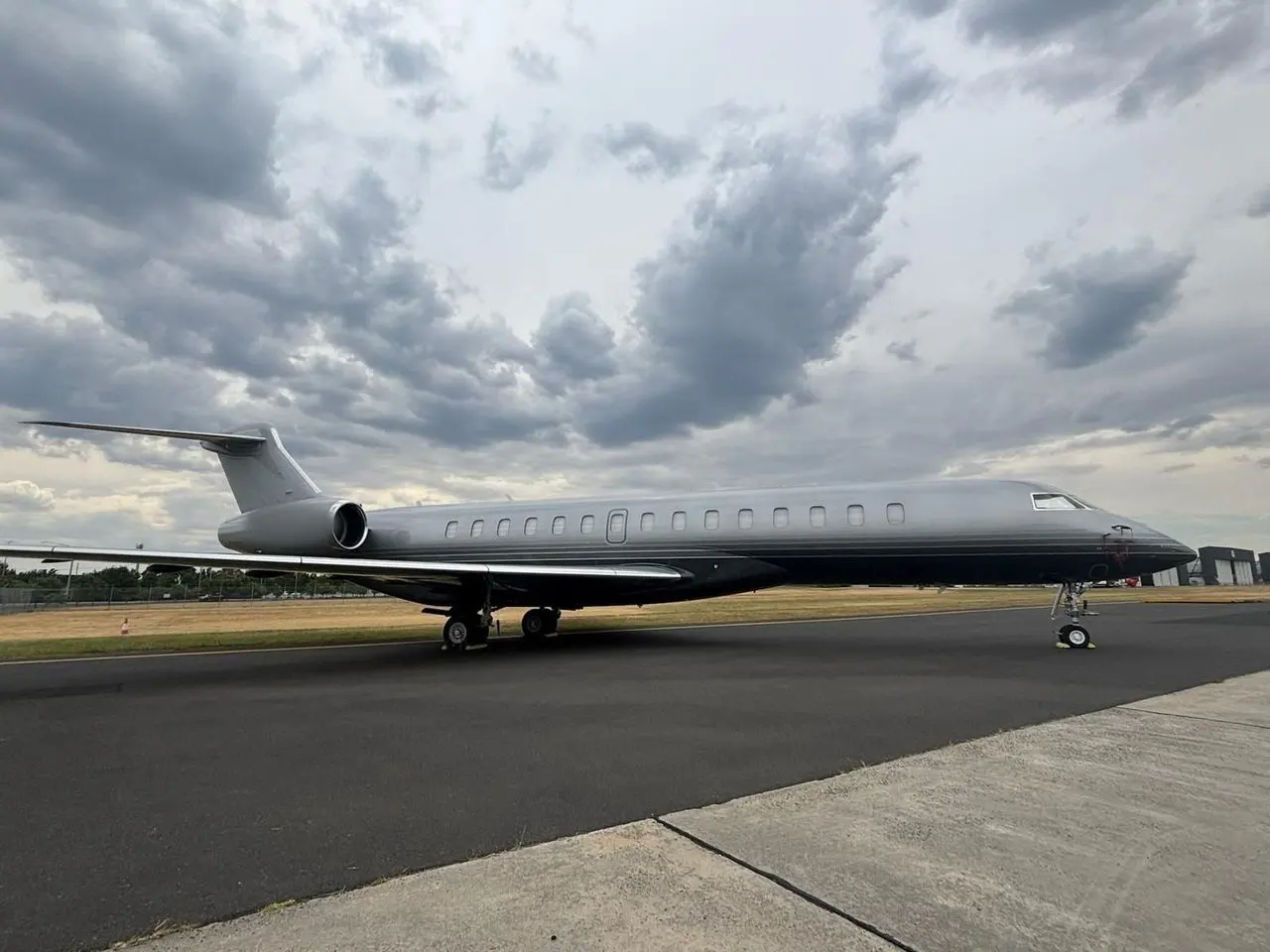 Large private jet parked beside the taxiway under heavy cloud