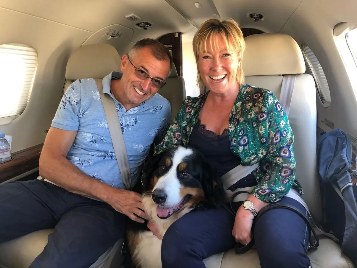 A smiling couple with their bernese mountain dog between them in a private jet cabin
