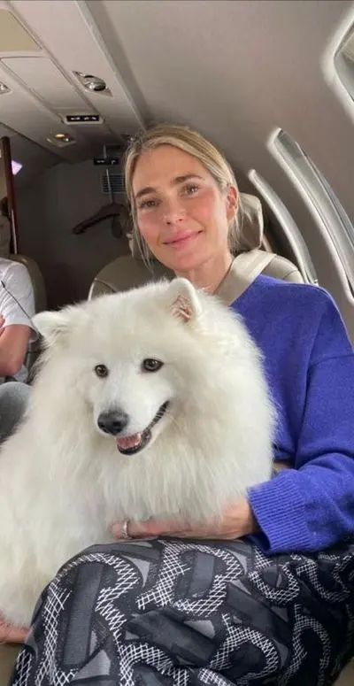 A fluffy white samoyed sitting on its owner’s lap in a private jet cabin