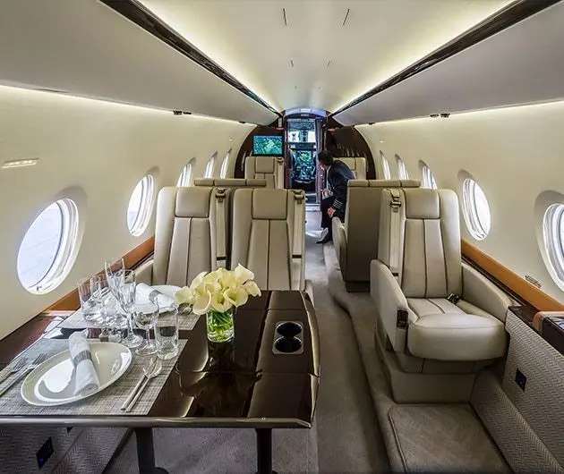 A private jet cabin with cream leather seats and a table set with glasses