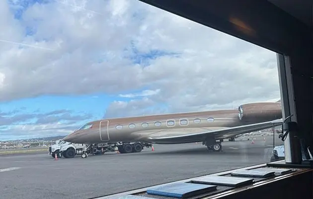 View from an open hangar door of a private jet parked on the apron
